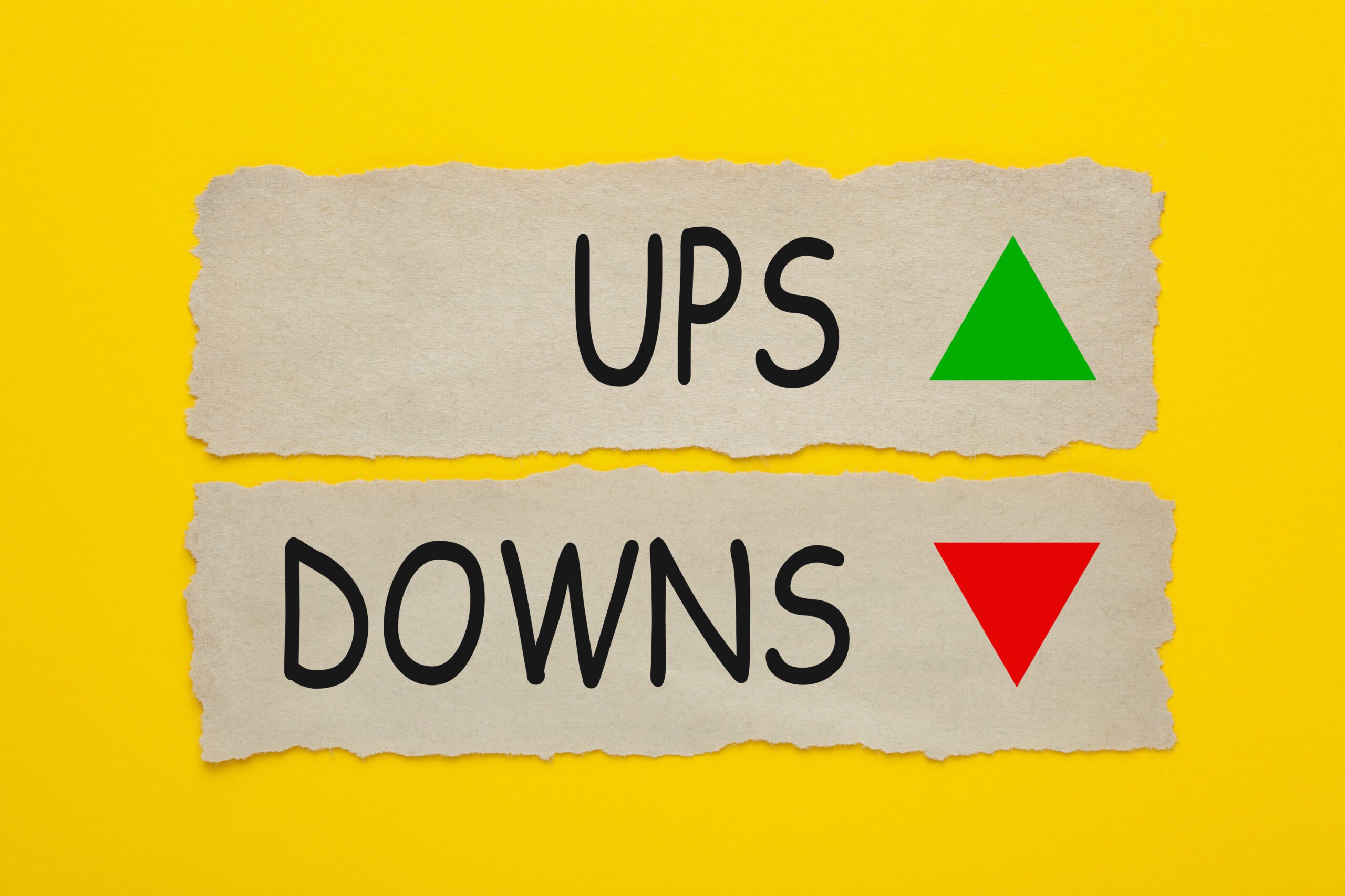 Ups And Downs written on old torn paper on yellow background. Two arrows 'up' and 'down'.